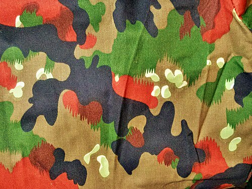 Close-up photograph of Swiss TAZ 83 Alpenflage camouflage fabric: a tan background with pale flecks, and green, red-brown and black leaf shapes.