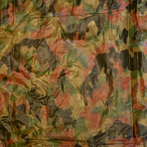 Rear of a Swiss Army rain poncho printed in the TAZ-83 Alpenflage pattern, shown on a white surface.