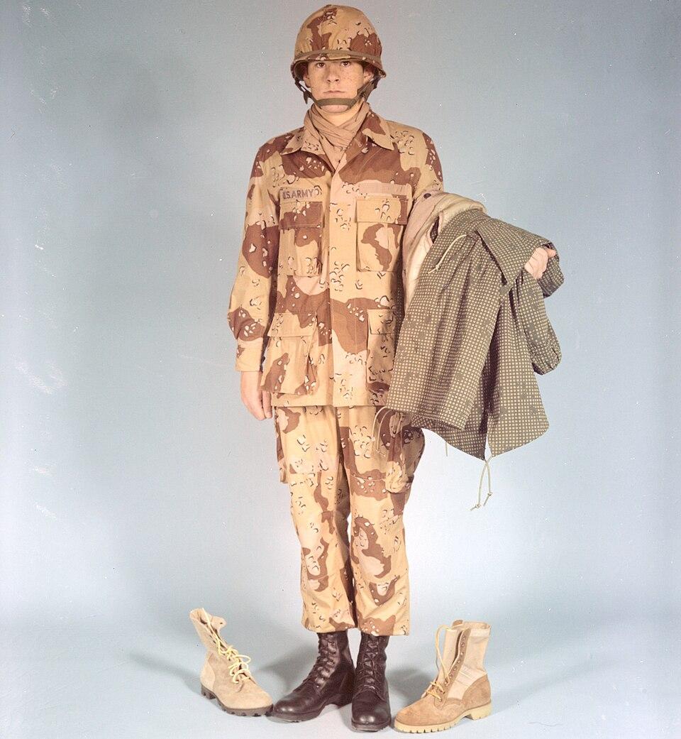 A 1976 US Army development photograph of a soldier in the 6-colour desert battle dress uniform holding the matching Desert Night Camouflage over-garment.