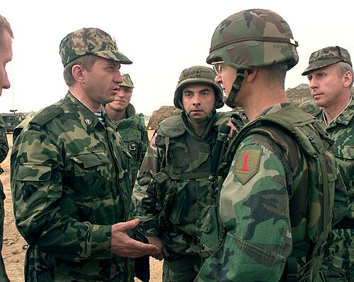 A Russian general in VSR/Dubok camouflage and field cap converses with a U.S. general and soldiers on a fortified position in Kosovo, 1999.