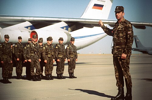 A Russian officer in a brown-dominant example of the vertically oriented Russian three-colour woodland pattern addresses his troops beside an Il-76 transport, Peacekeeper 95.