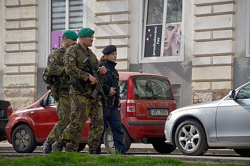 Two Czech soldiers in vz.95 leaf camouflage with green berets patrol a Brno street with a police officer following the 2016 Brussels attacks.