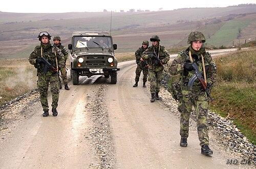 Czech soldiers wearing vz.95 leaf camouflage on a KFOR patrol in Kosovo, passing a Land Rover with MO CR (Czech MOD) markings.