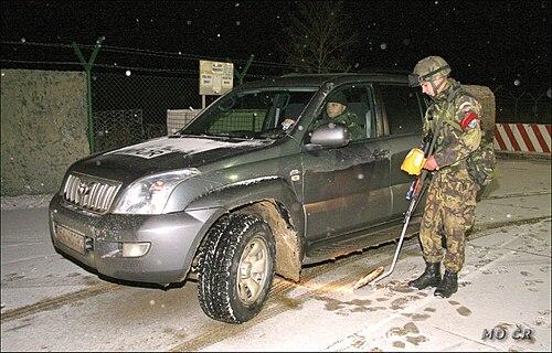 A Czech soldier in vz.95 leaf camouflage operating a mine detector beside a vehicle at night during the KFOR mission.