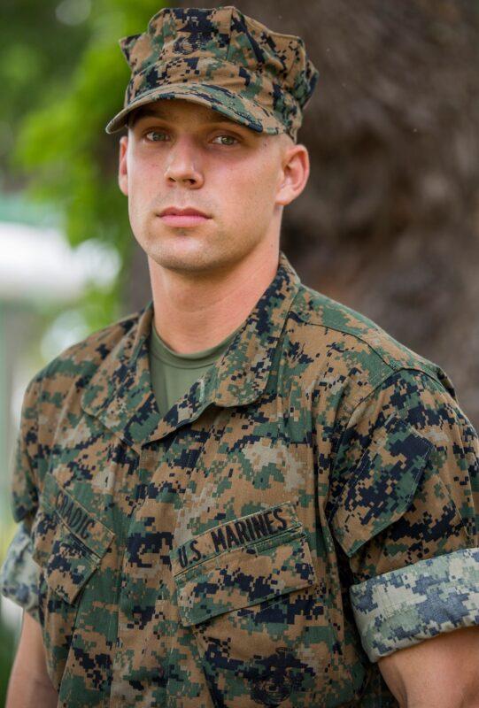 Head-and-shoulders portrait of a U.S. Marine recruit wearing a green-and-black pixelated woodland camouflage utility blouse with a name tape.