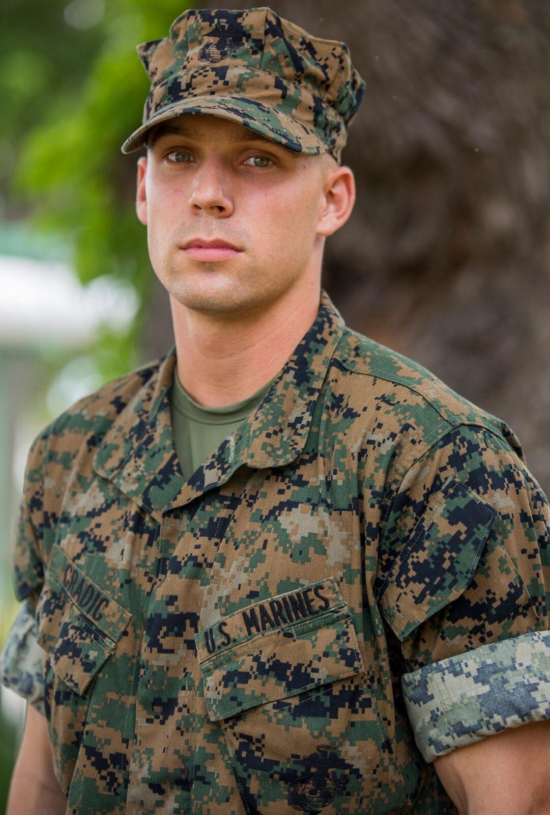 Head-and-shoulders portrait of a U.S. Marine recruit wearing a green-and-black pixelated woodland camouflage utility blouse with a name tape.