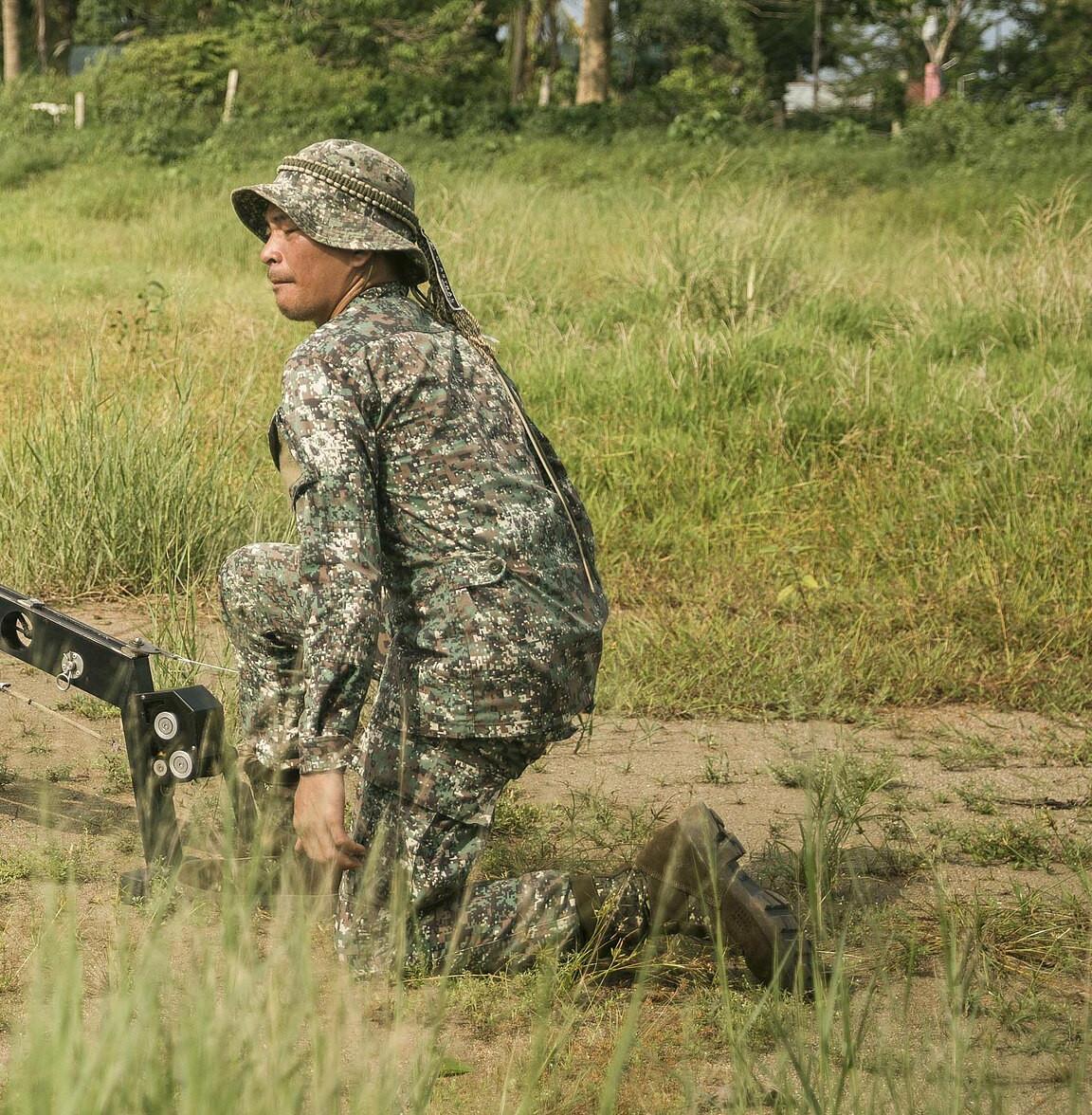 A kneeling Philippine Marine in a pale grey-green fine-grid digital camouflage uniform and boonie hat at the launch position of a small unmanned aircraft in an open field; the aircraft itself is not visible in the frame.
