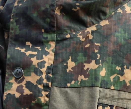 Detail crop from a field photograph: the camouflaged jacket panel and pocket flap of a Russian internal troops special purpose unit serviceman, showing small straight-edged shapes with pointed corners on dark green cloth.