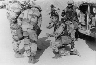 A kneeling U.S. colonel conferring with liaison officers of the French 6th Light Armored Division in front of a rocky hillside, January 1991 — recorded small and in black and white, so no garment is resolvable.