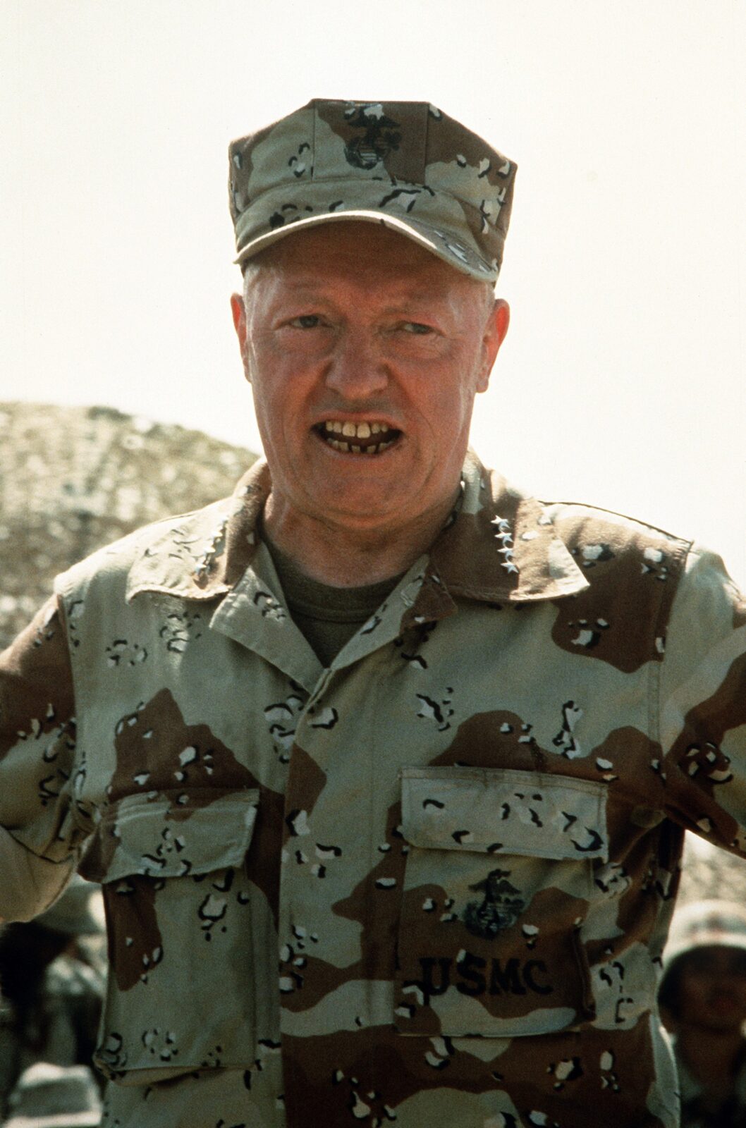 Portrait-format photograph of the Commandant of the Marine Corps briefing Marines in Saudi Arabia, wearing six-colour desert camouflage.