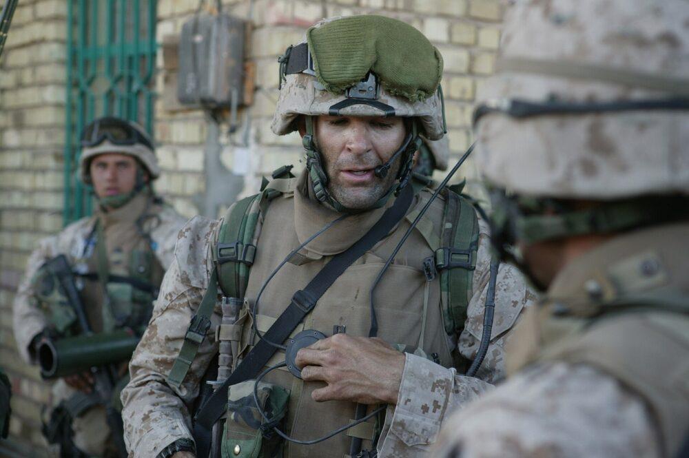 A U.S. Marine officer with a radio handset, wearing a sand-coloured pixel camouflage uniform and a helmet with a matching cover.