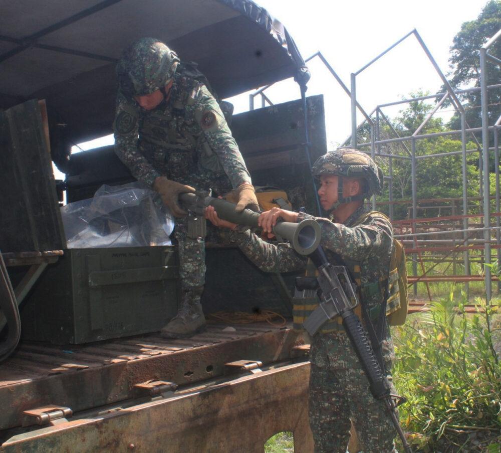 Two Philippine Marines in green square-block digital camouflage handling a shoulder-fired anti-tank launcher beside a truck; the institutional page emblem present in the source photograph is not included in this cropped version.