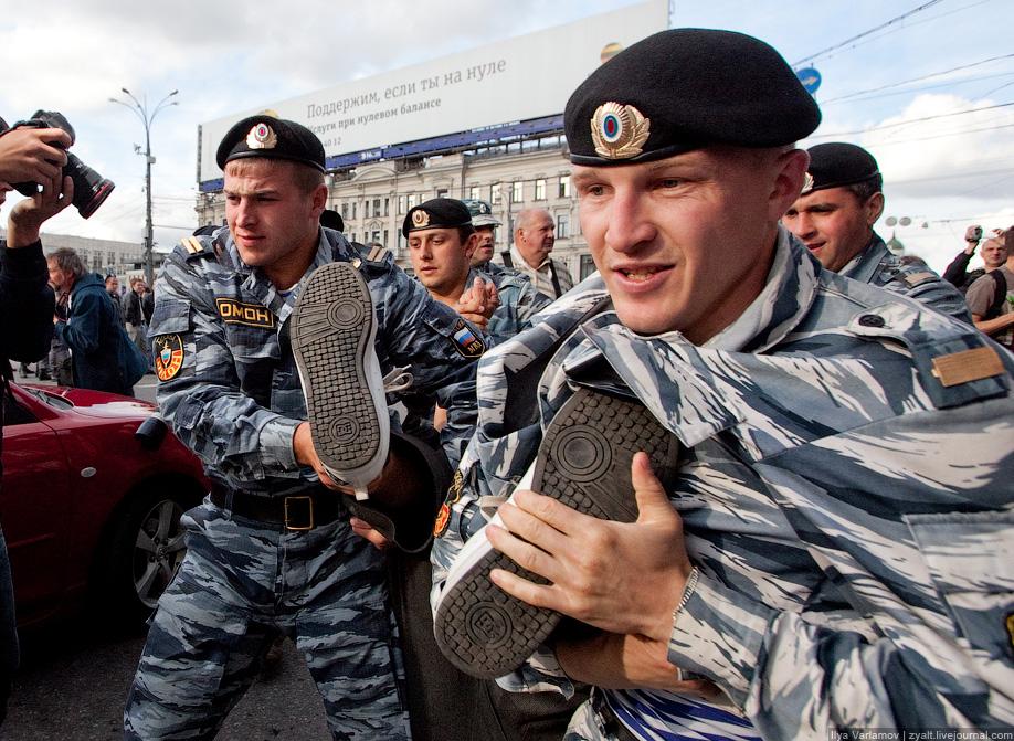 Two standing police officers in pale blue-white-grey wavy-striped camouflage uniforms, each holding a boot, in a city street.