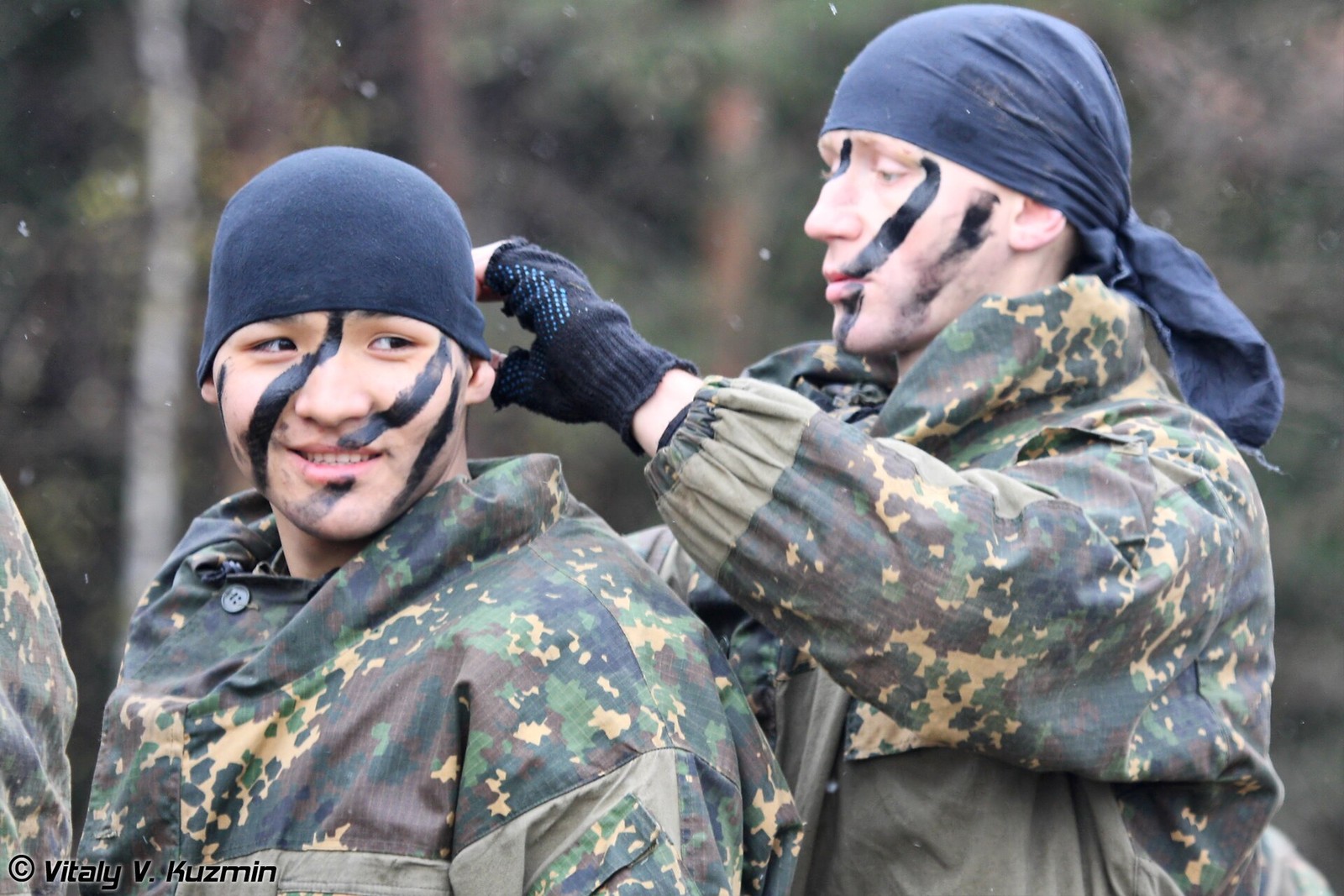 Two Russian internal troops special purpose unit servicemen in camouflage, one adjusting the other’s headgear, photographed at an exhibition.