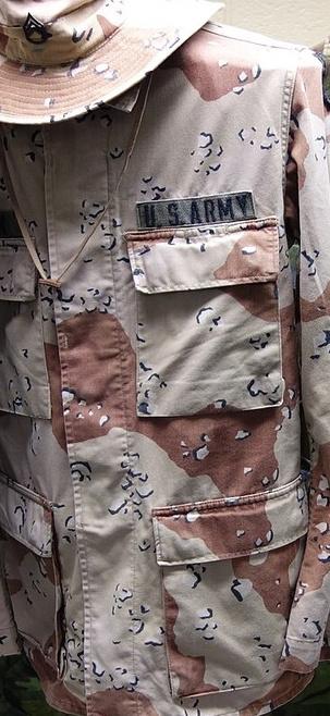 Six-colour desert-pattern jacket with a matching bush hat and a U.S. ARMY chest tape, on a mannequin stand in a museum display of US Army camouflage patterns.