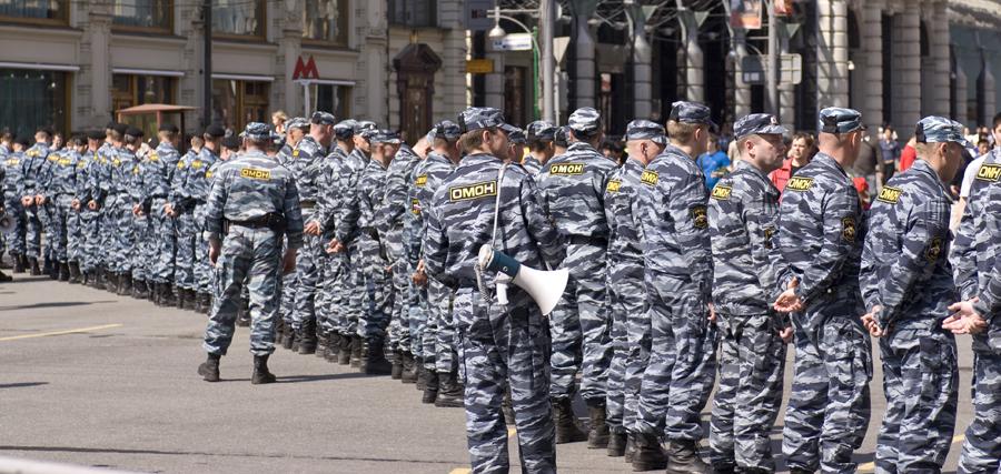 A long line of police officers in pale blue-grey camouflage, all in printed soft caps, photographed from behind in a city street.