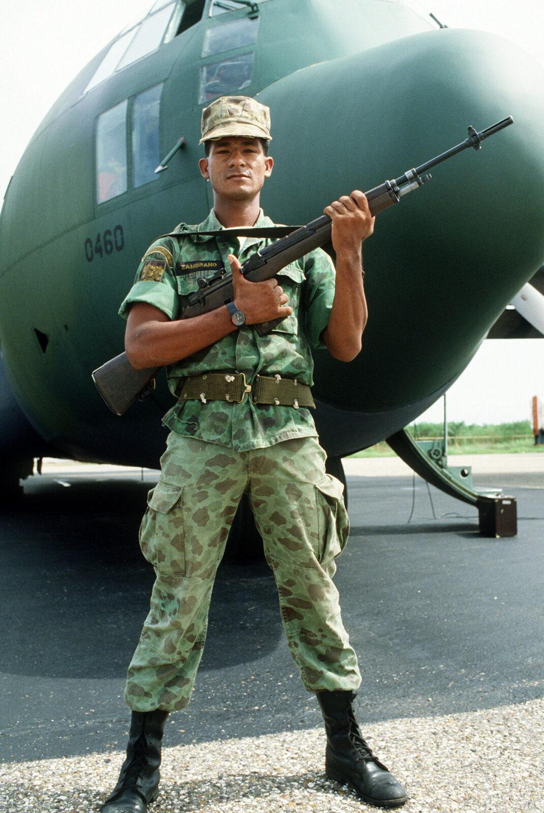 A soldier in camouflage uniform standing guard in front of a transport aircraft, holding a rifle.