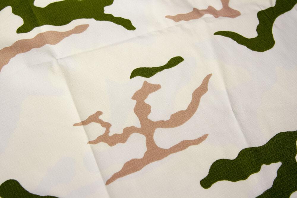 Close-up of Tundra camouflage fabric: a white ground with dark green and salmon-pink irregular shapes across a fold in the cloth.