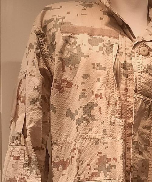 Estonian desert digital camouflage jacket — sleeve, chest and lower pockets — on a mannequin, the sand-ground three-colour pixelated fabric filling most of the frame.