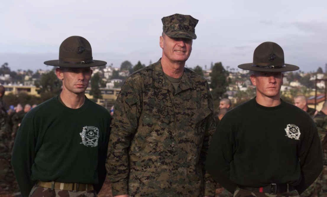 A U.S. Marine general in a prototype pixel camouflage uniform standing between two drill instructors in campaign hats and green shirts.