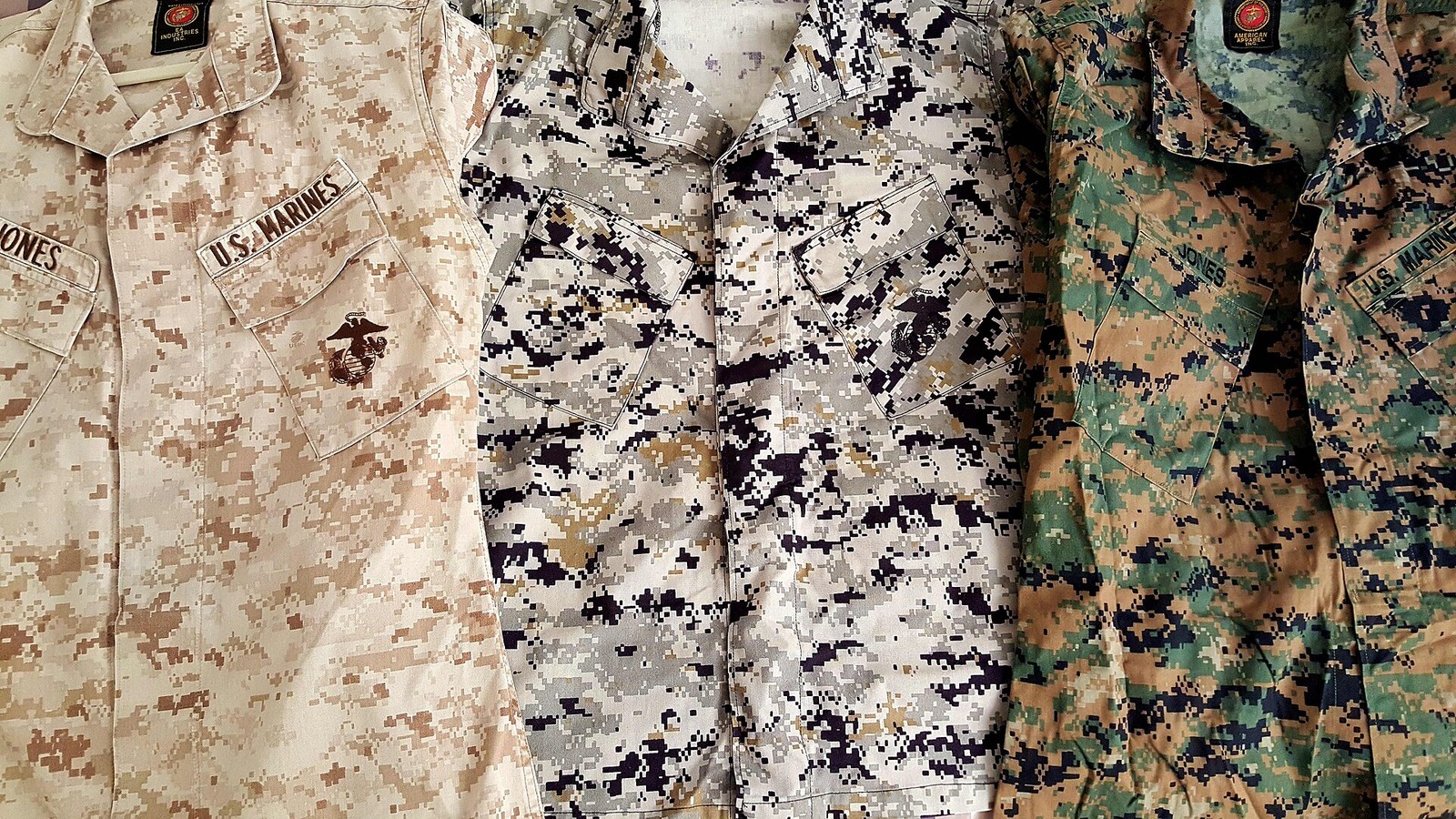 Three camouflage utility uniforms laid out side by side in sandy, grey and green pixel patterns.