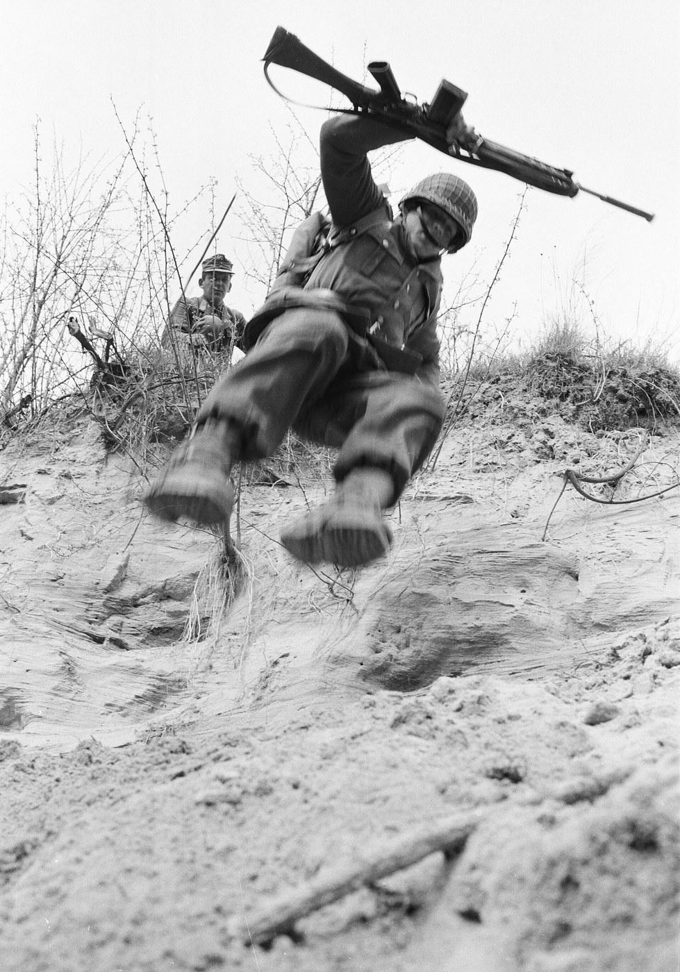 An Austrian Bundesheer recruit in Erbsentarn camouflage sliding down a slope during basic training with a Sturmgewehr 58 at Mistelbach, 1967.
