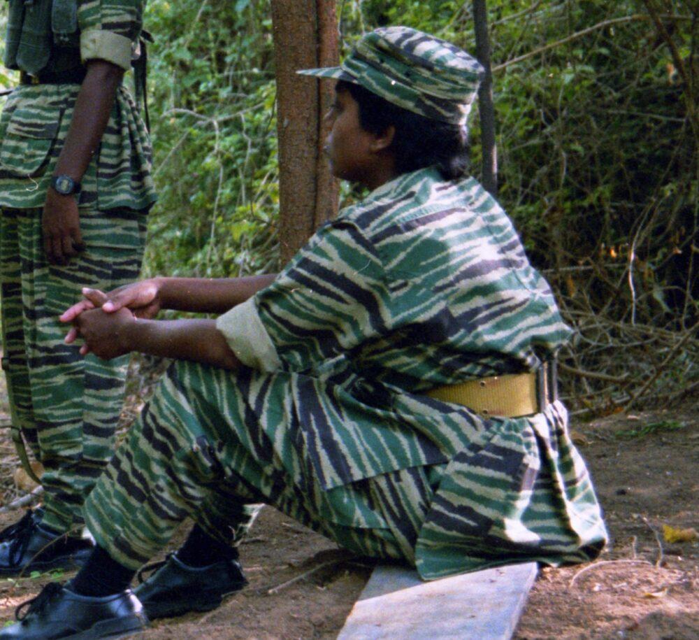Close view of LTTE camouflage uniform fabric: horizontal spiny stripes in green, dark green and pale khaki, with a khaki webbing belt, folds and shadows