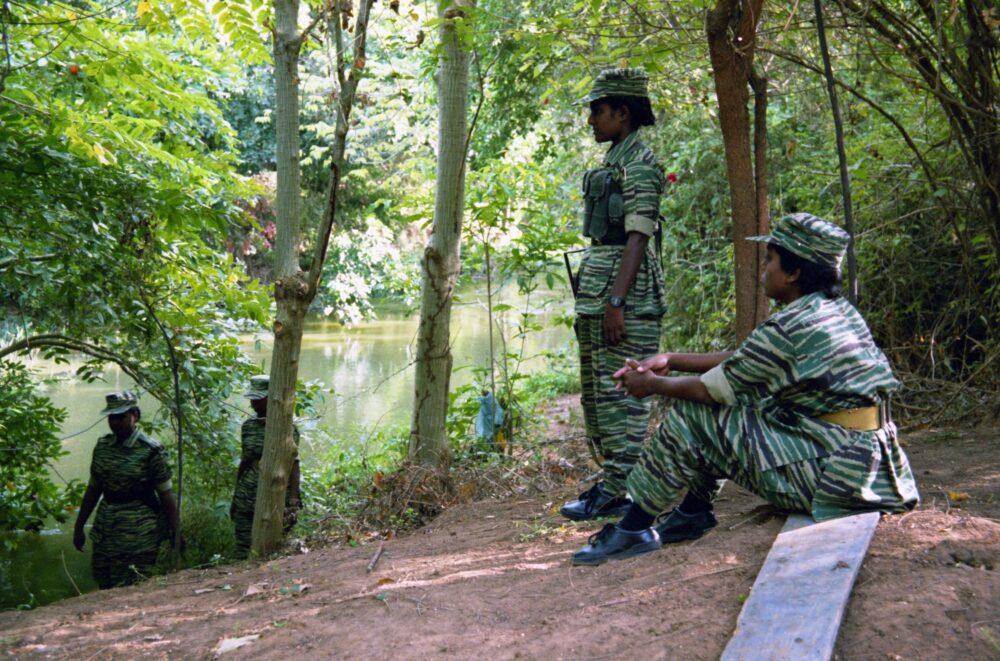 LTTE cadres in spiny-stripe camouflage uniforms beside a river crossing in northern Sri Lanka, 2002, one standing and one seated