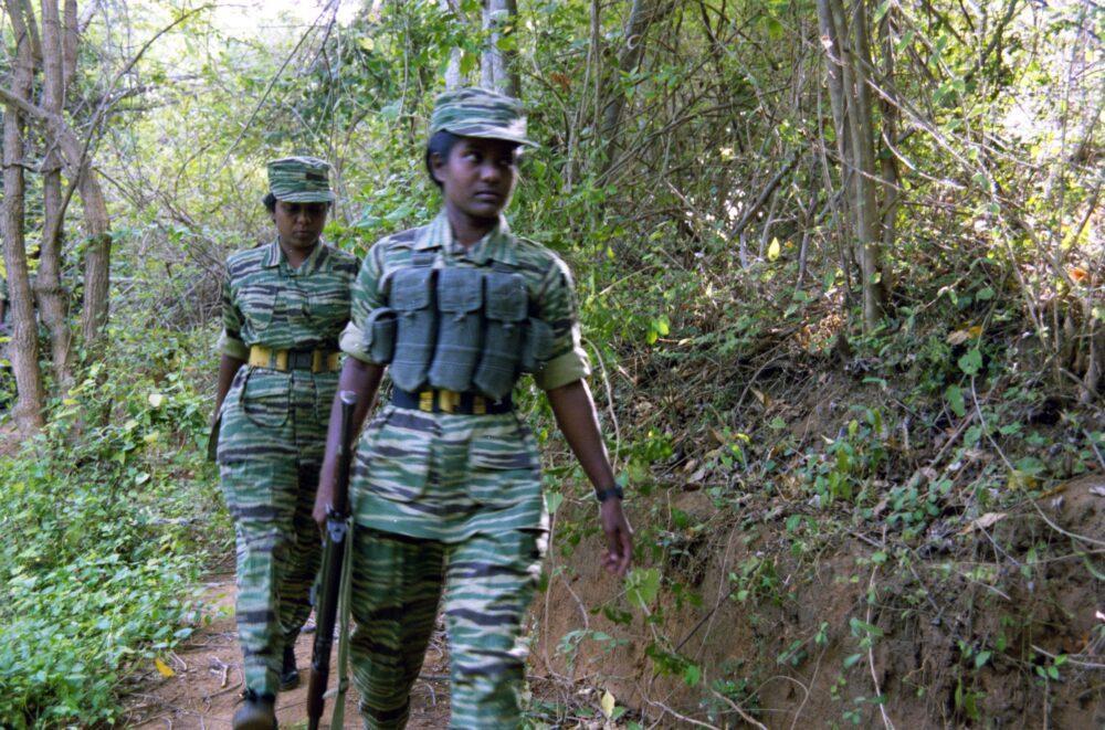 Two LTTE women cadres walking a jungle path in northern Sri Lanka in 2002, wearing camouflage uniforms with horizontal spiny stripes in green, dark green and khaki