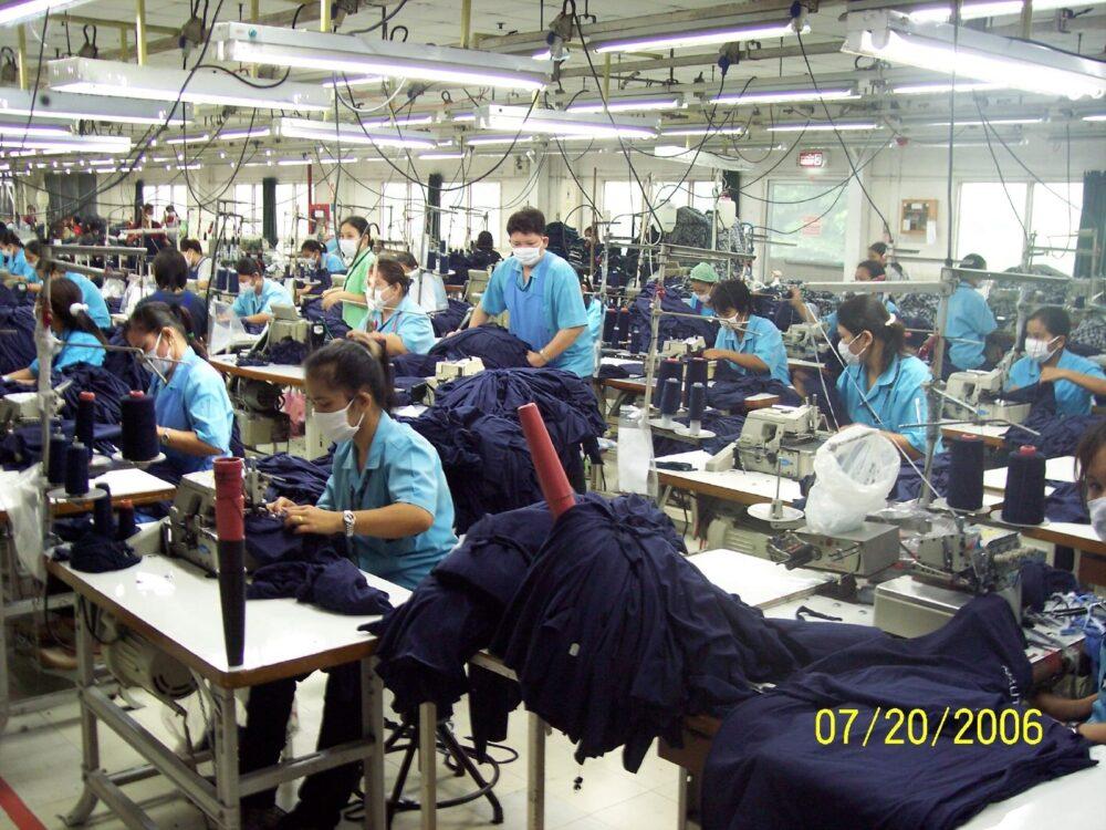 A row of industrial sewing machines with operators in a garment factory