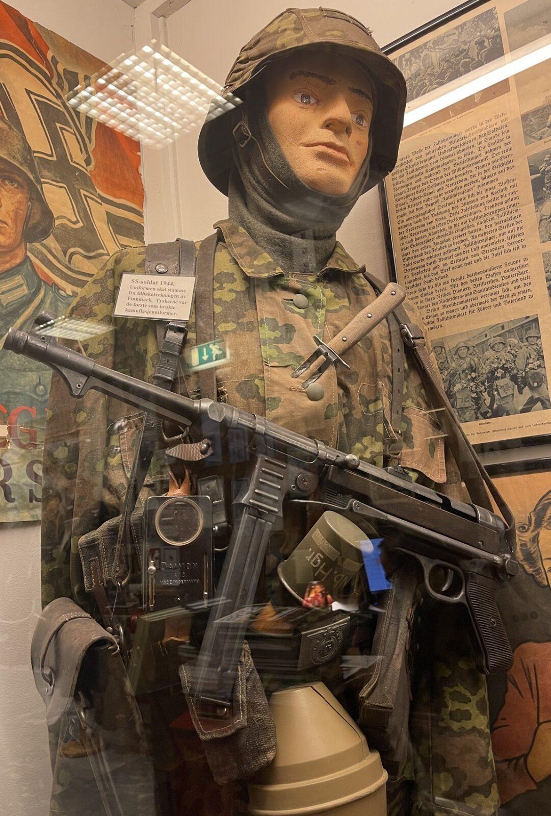 Museum display figure wearing a printed camouflage jacket, matching trousers and helmet cover with an MP 40, Lofoten War Memorial Museum, Norway