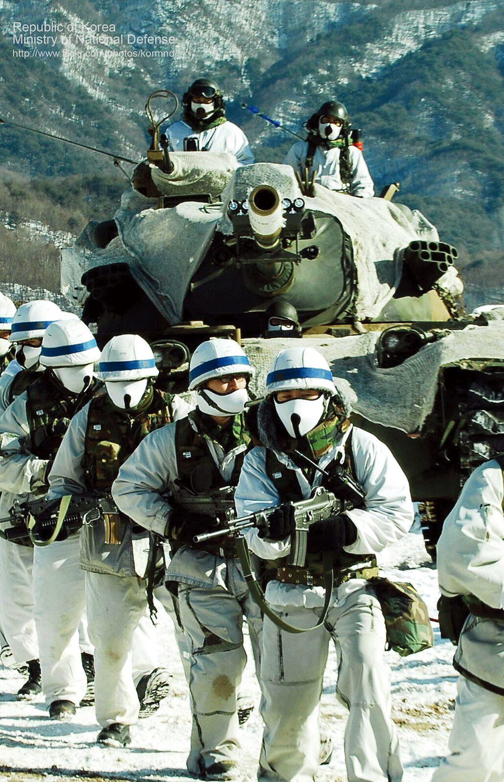 Republic of Korea Army soldiers in white winter oversuits moving past a tank during cold-weather training, January 2008