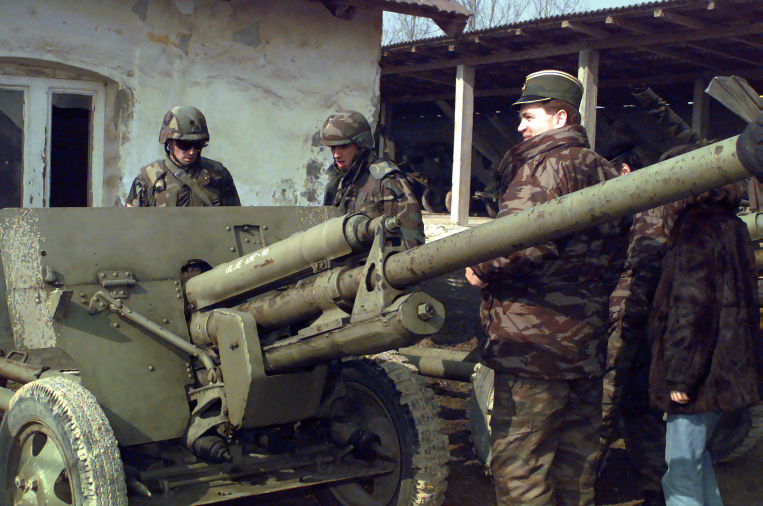 Serbian officer in camouflage uniform showing US soldiers a towed anti-tank gun, 1999