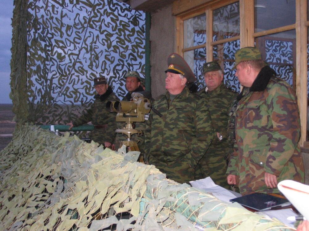 Russian officers in the Flora (VSR-98) field uniform at an observation post during exercises: green field jackets printed with dark green and brown marks in horizontal bands, spotting scopes and camouflage netting around them, April 2007