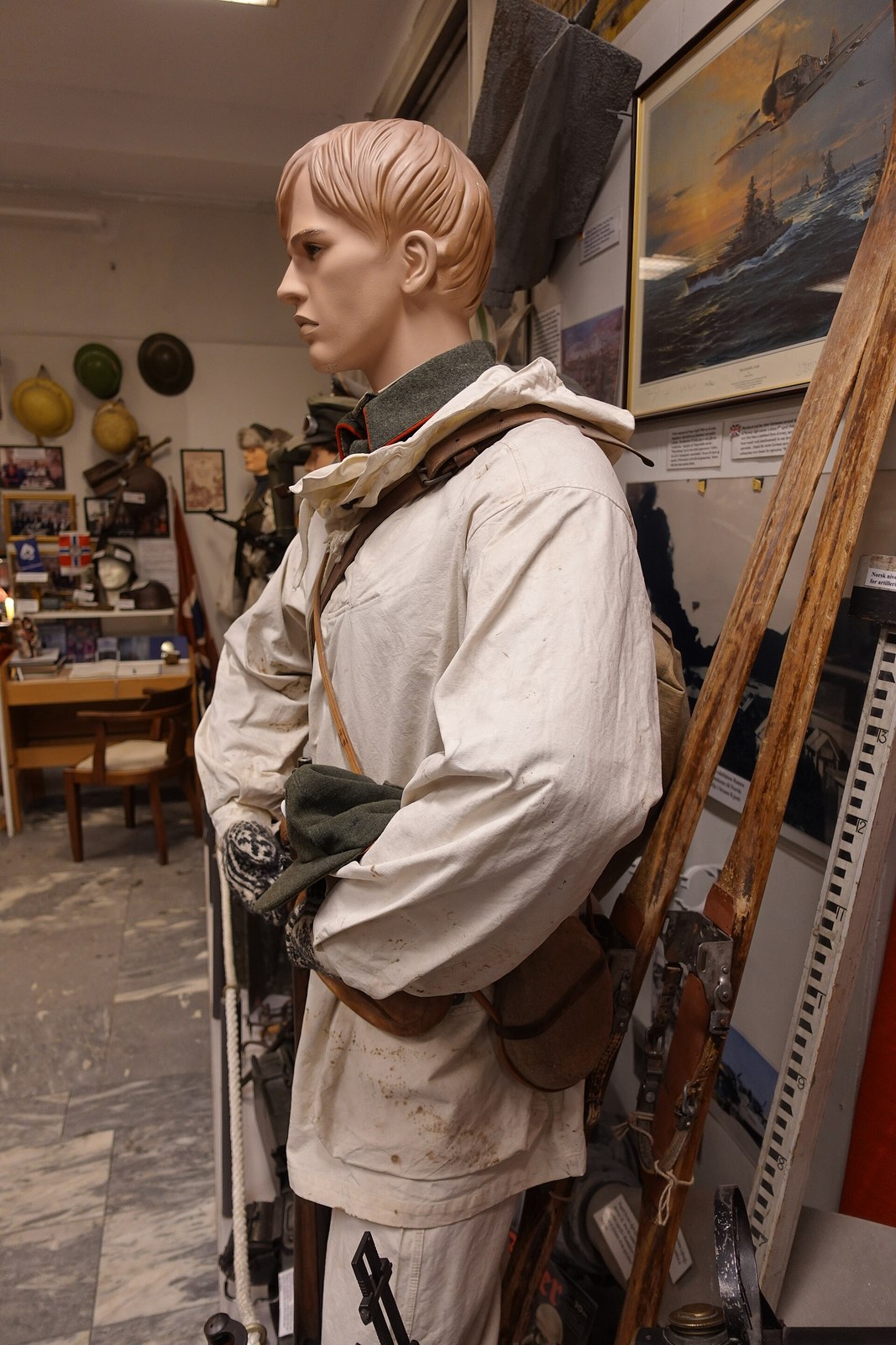Norwegian Army white snow camouflage smock worn over a grey field uniform by a museum mannequin, with wooden skis and a framed painting behind