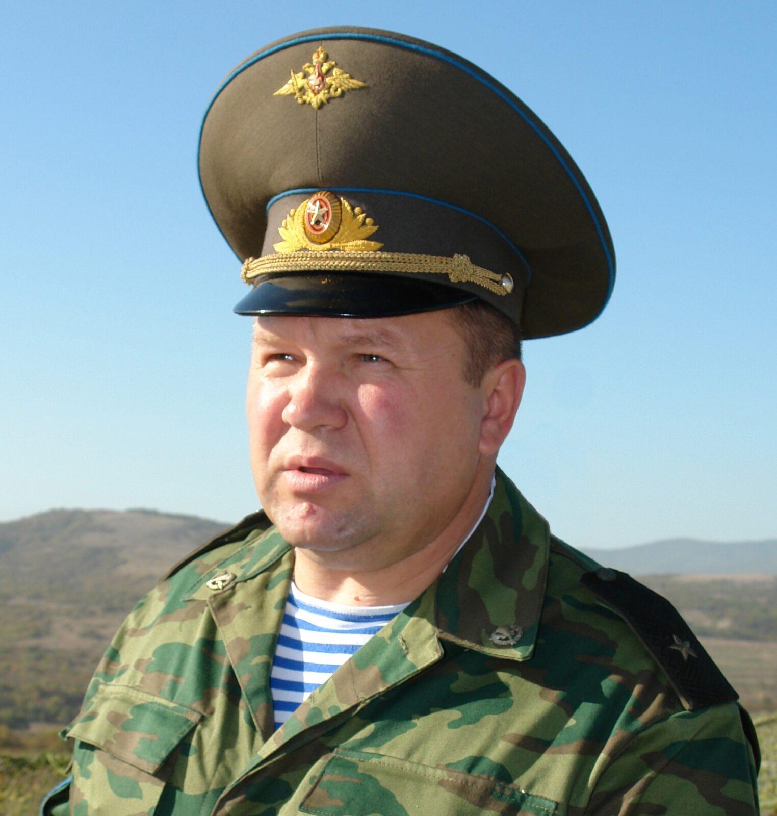 Russian airborne major general in the Flora (VSR-98) field uniform: a pale khaki-green jacket printed with dark green and brown marks arranged in horizontal bands, worn over a blue-and-white striped telnyashka, with a peaked cap bearing the airborne emblem